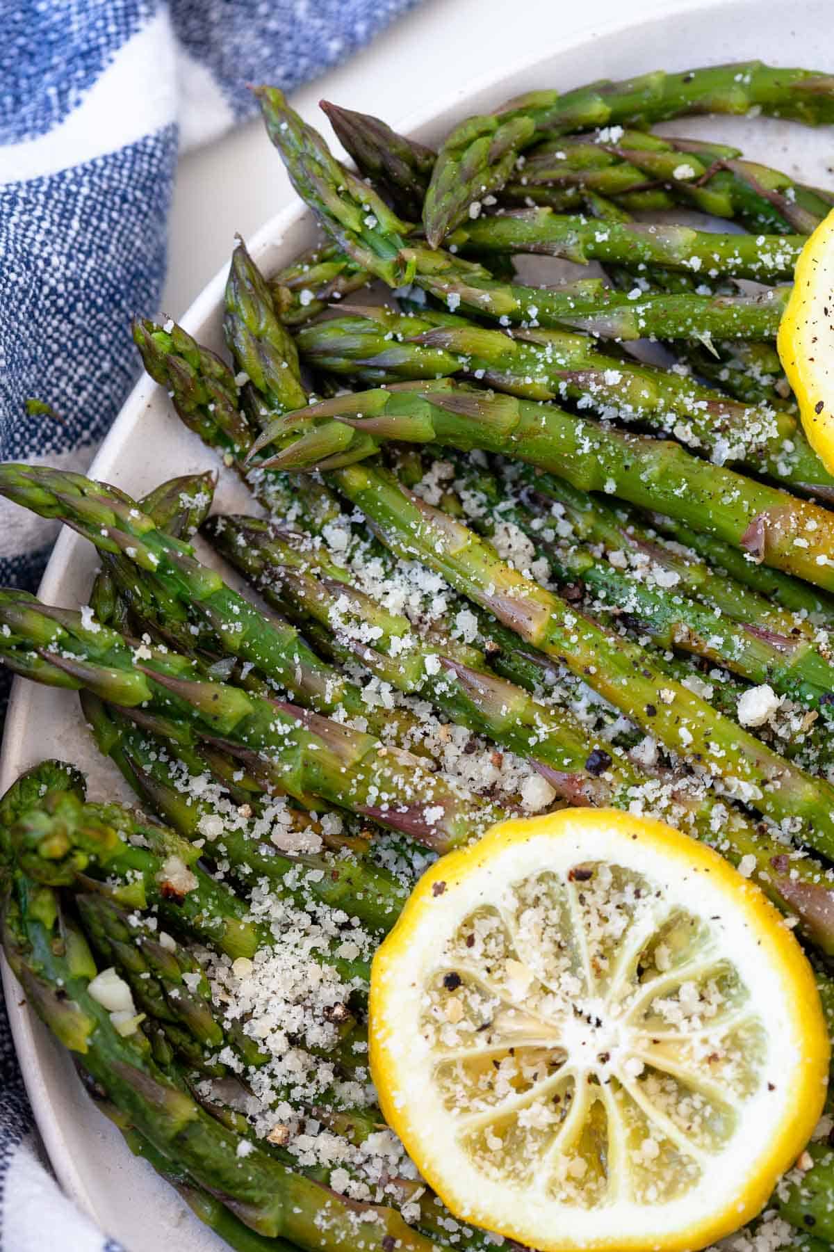 green asparagus in white bowl with lemons on white background, blue striped napkin