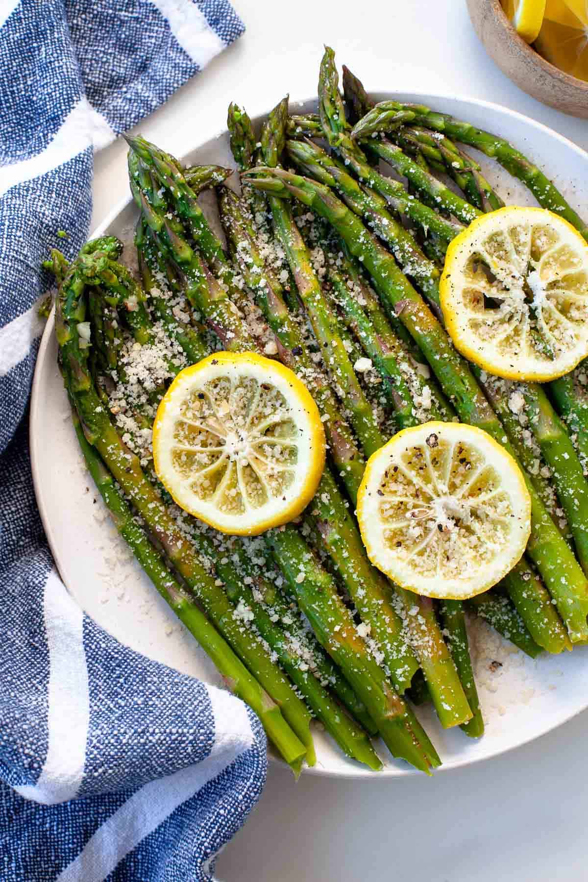 green asparagus in white bowl with lemons on white background, blue striped napkin