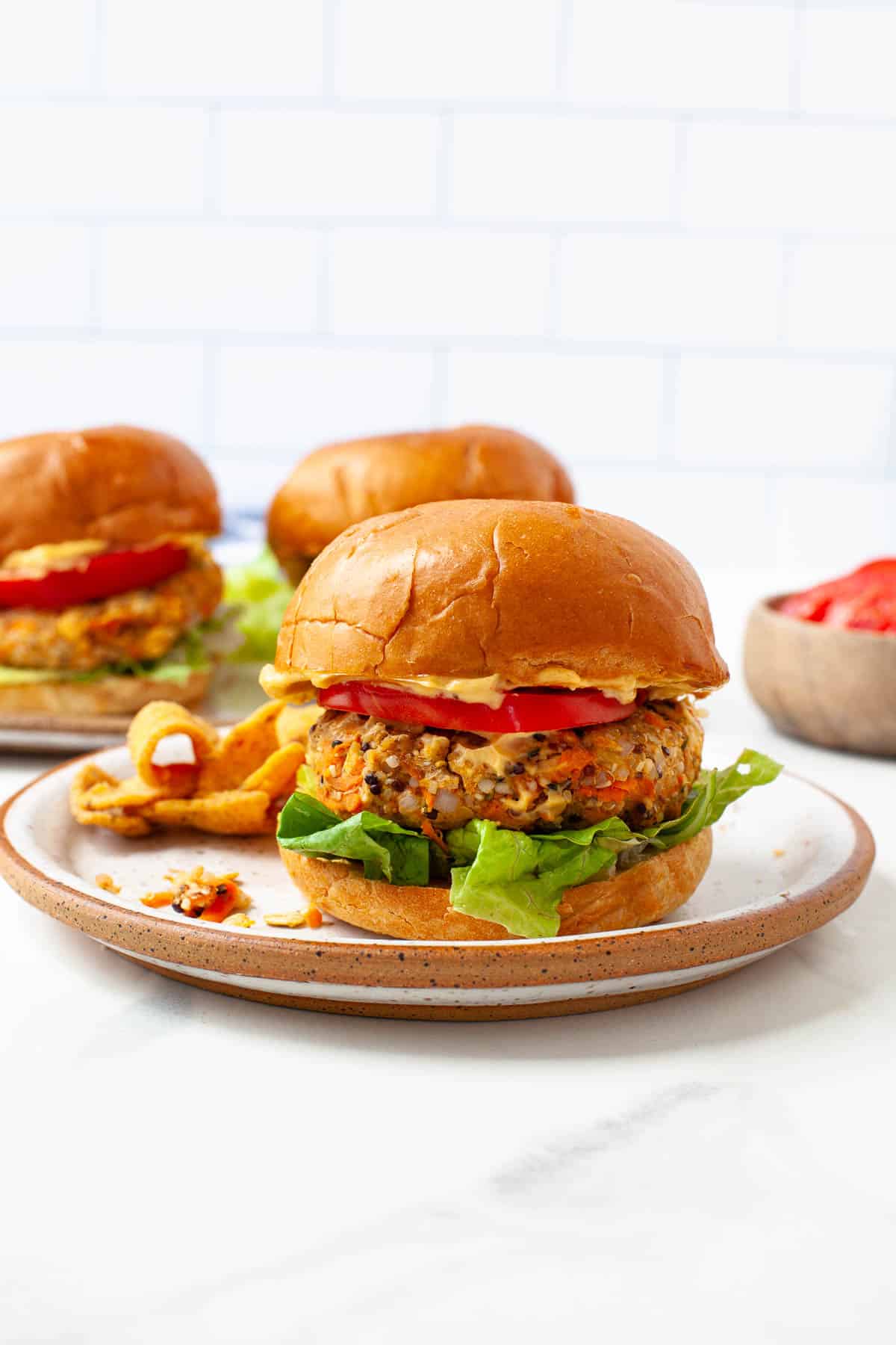 vegan chickpea burger on bun with lettuce, tomato, vegan aioli with two burgers behind