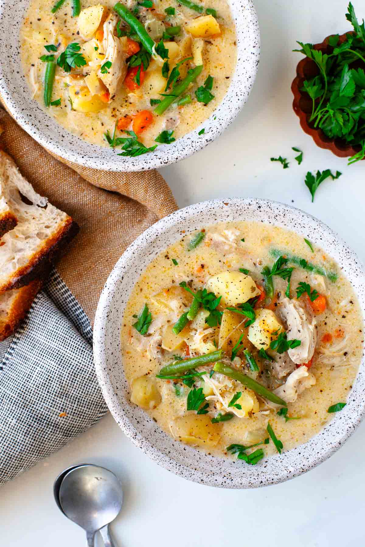 Two bowls of Instant Pot Chicken Stew garnished with fresh parsley beside two silver spoons and a kitchen towel