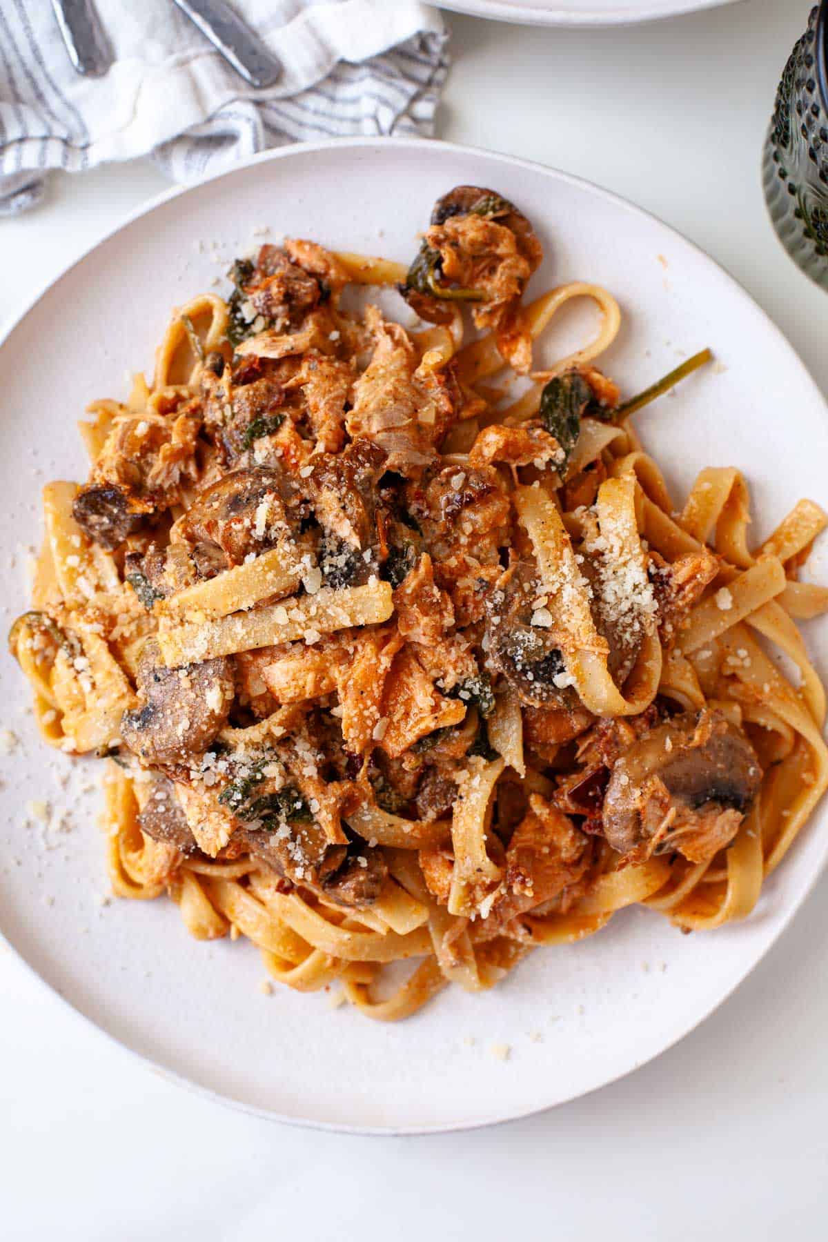 blackened salmon pasta topped with grated parmesan cheese on white plate.