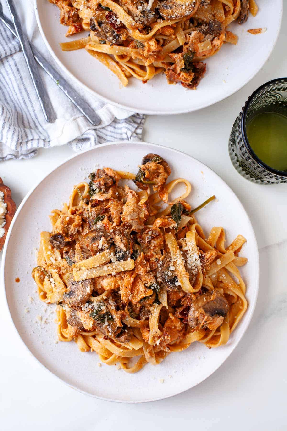 two plates of blackened salmon pasta topped with grated parmesan cheese.